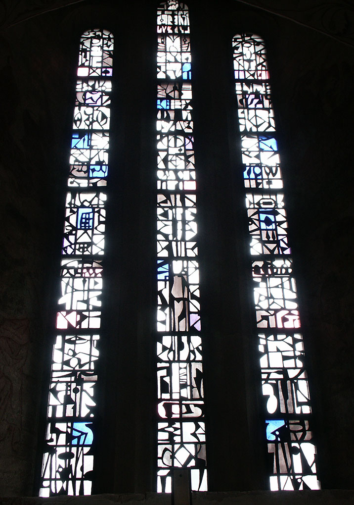 Tall, narrow stained-glass windows filled with abstract geometric shapes in white, black, and touches of blue and purple, glowing with daylight.
