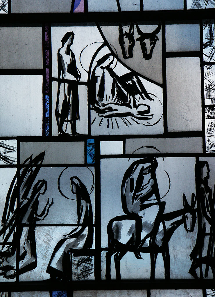 Stained-glass window with black line art depicting biblical scenes, including a manger, haloed figures, an angel, and travelers with a donkey.