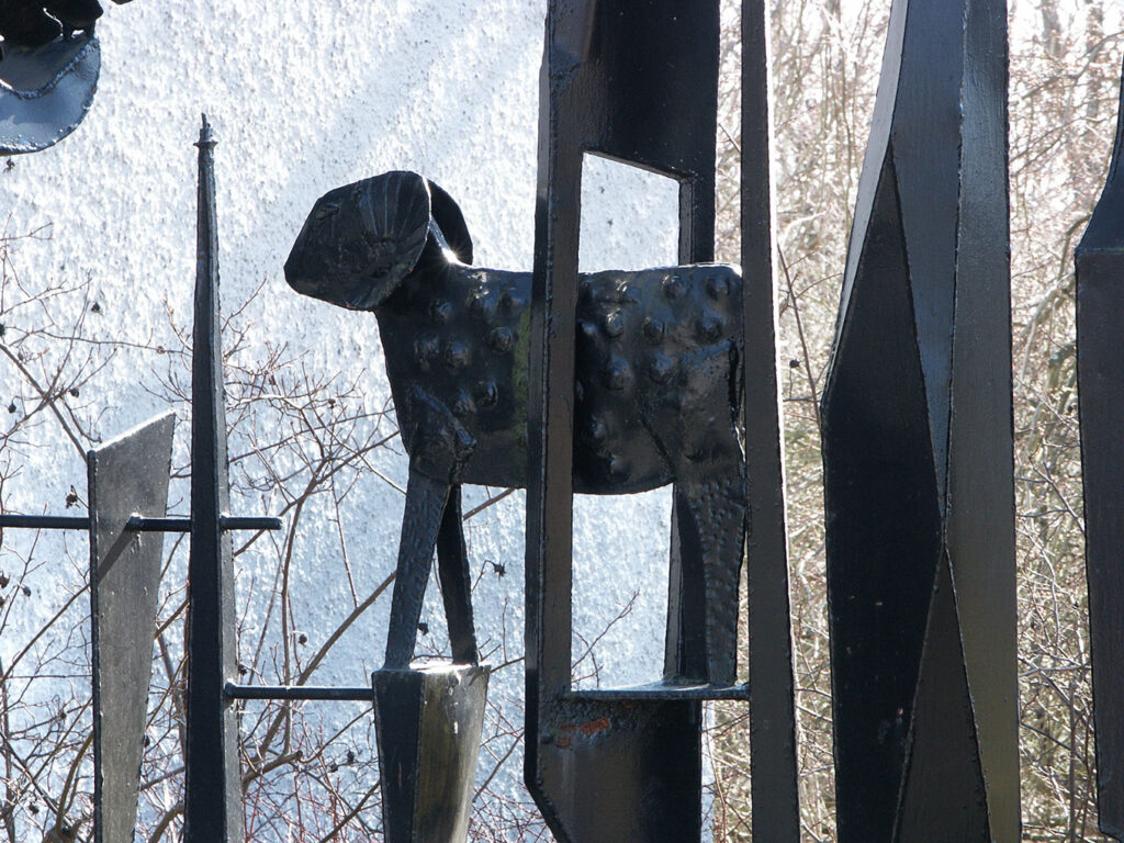 Close-up of a black metal sculpture featuring a textured, stylized animal figure framed by vertical metal elements outdoors.