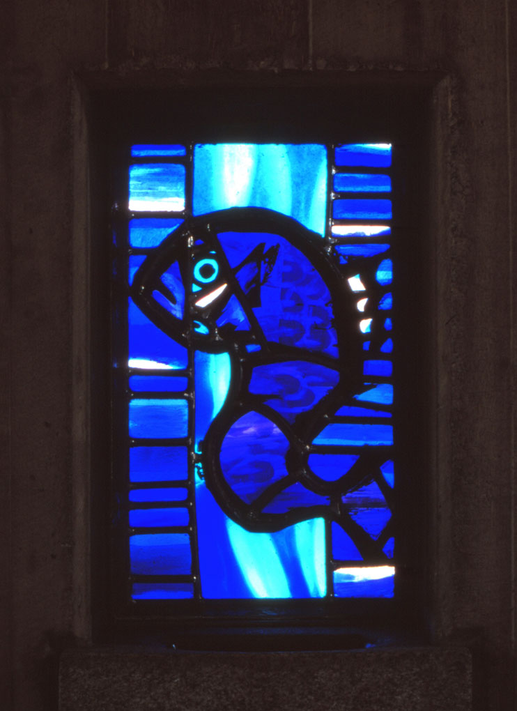 Bright blue stained-glass window depicting an abstract fish-like figure outlined in dark lead against vivid layered blue and turquoise glass.