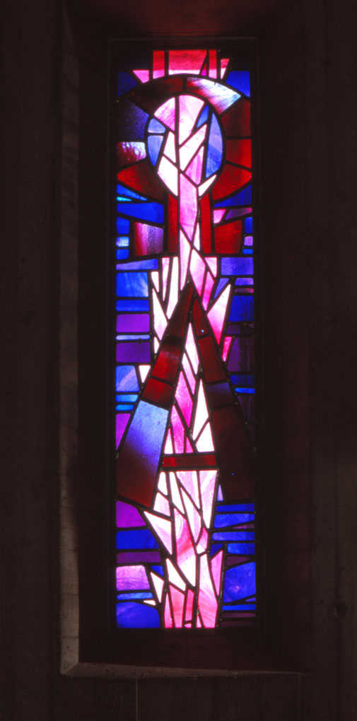 Tall stained-glass window in vivid red, pink, and blue tones forming an abstract standing figure with geometric shapes and radiant light.
