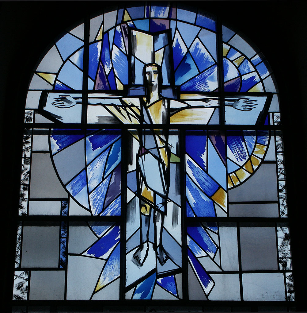 Stained-glass window depicting an abstract crucifix figure with outstretched arms, surrounded by vibrant blue and yellow geometric shapes.