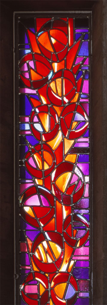 Vibrant stained-glass window with circular red, orange, and purple geometric shapes arranged vertically, glowing with warm light.