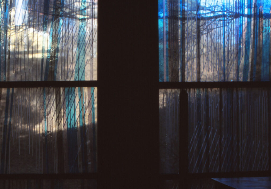 Abstract blue-toned stained glass windows with vertical streaks of color set in dark frames, showing soft light filtering through.