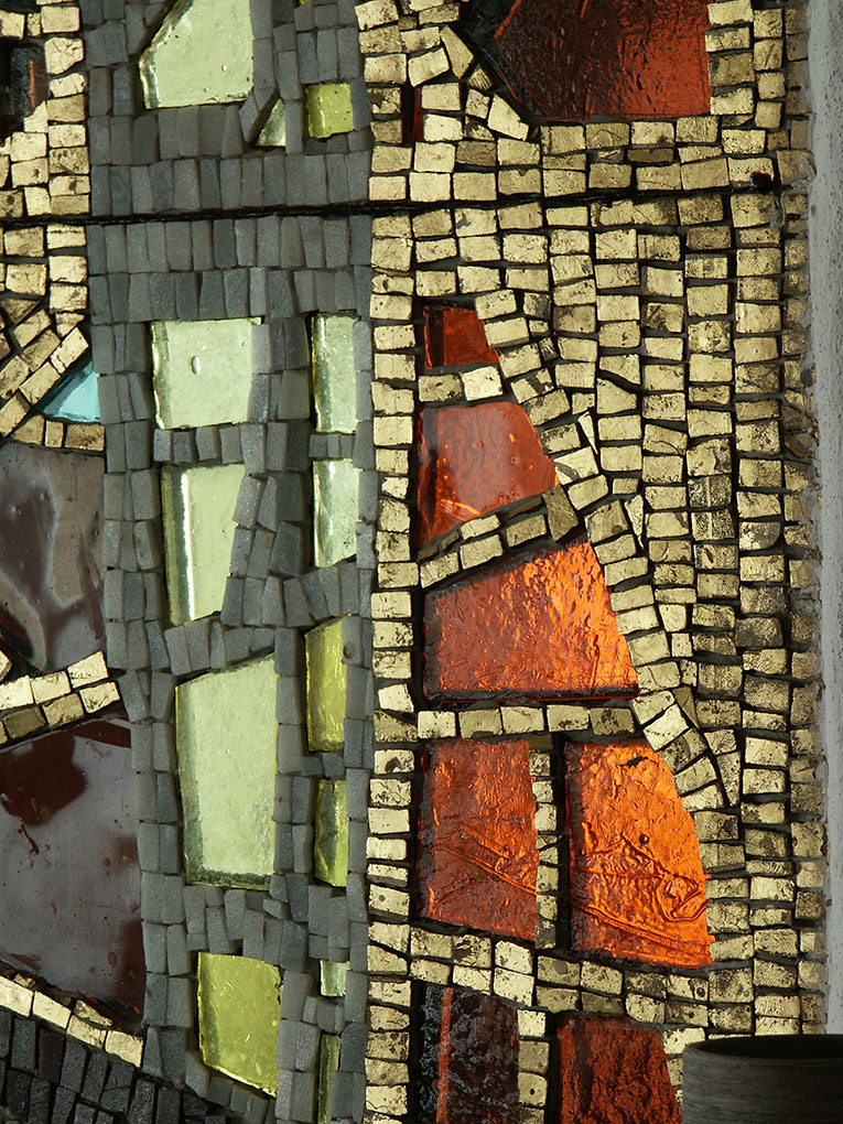 Mosaic detail with gold, gray, and vibrant orange and green glass pieces arranged in angular patterns on a textured surface.