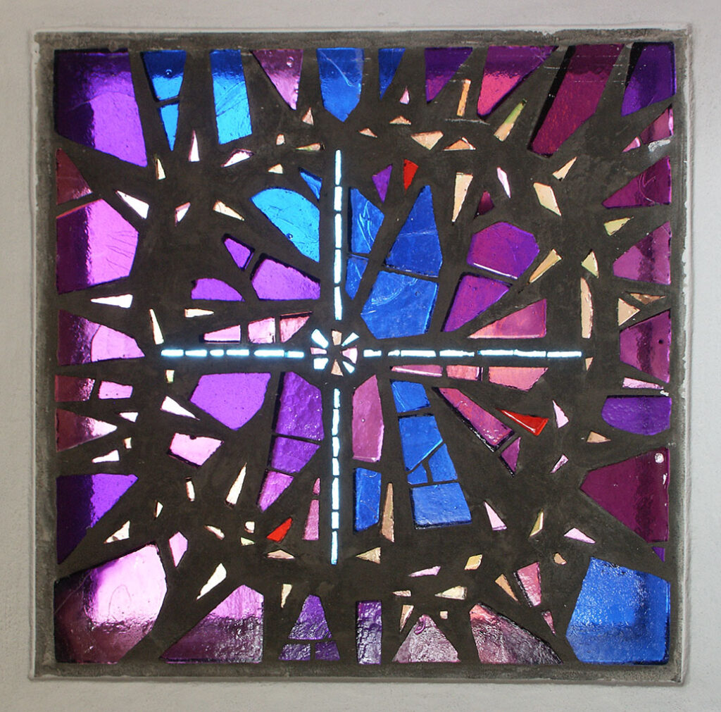 Stained-glass window with a bright cross at the center, surrounded by sharp purple, blue, and pink geometric shapes in a square frame.