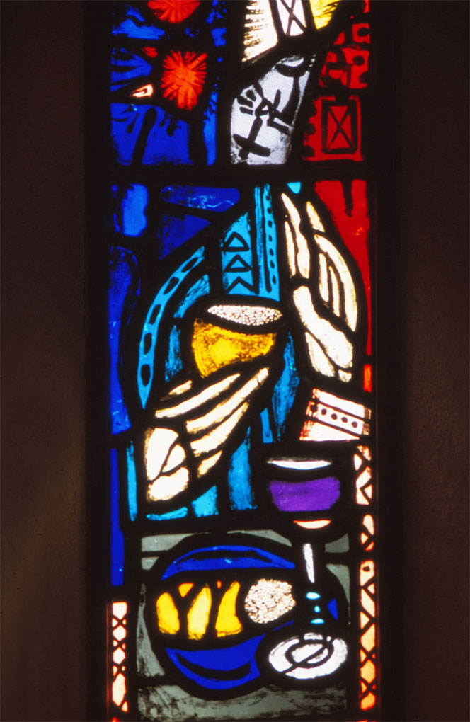 Stained-glass panel with vivid blue, red, and yellow tones showing hands holding a cup, a plate of bread, and a chalice in abstract form.