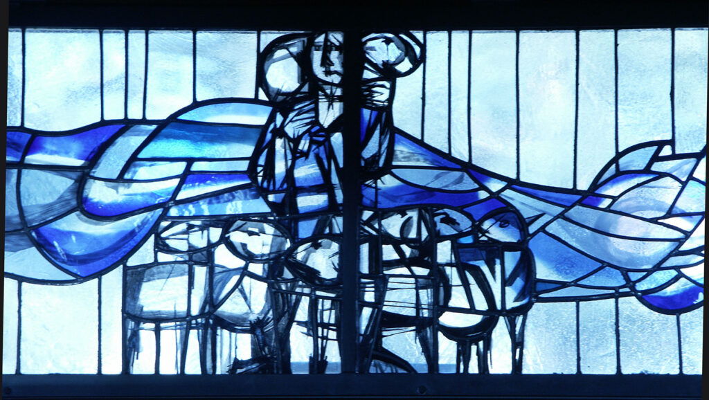 Blue-toned stained glass window showing an abstract central figure standing above a group of stylized people with flowing wave-like shapes behind.