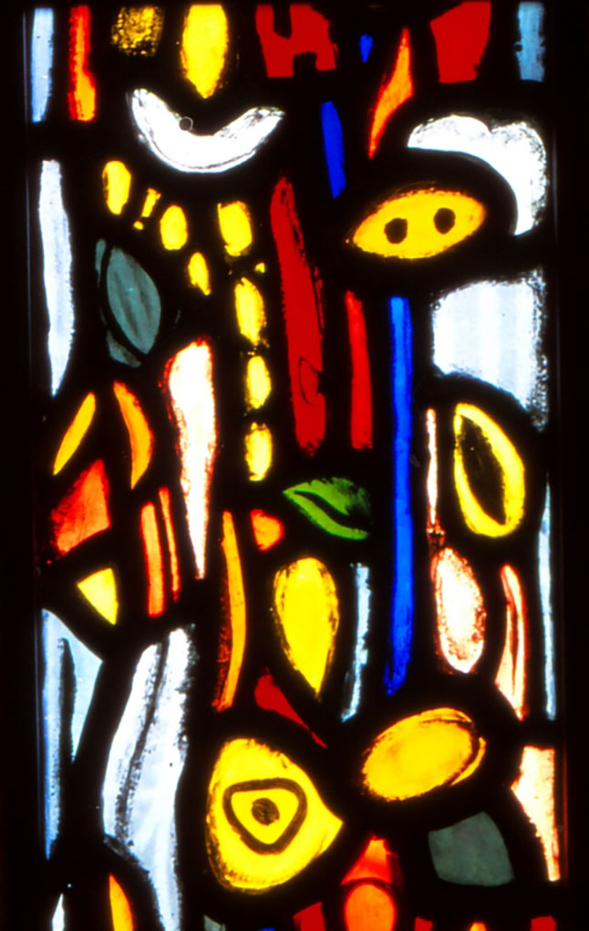 Colorful abstract stained-glass panel with bright yellow, red, blue, and white shapes, leafy motifs, and bold black leading throughout.