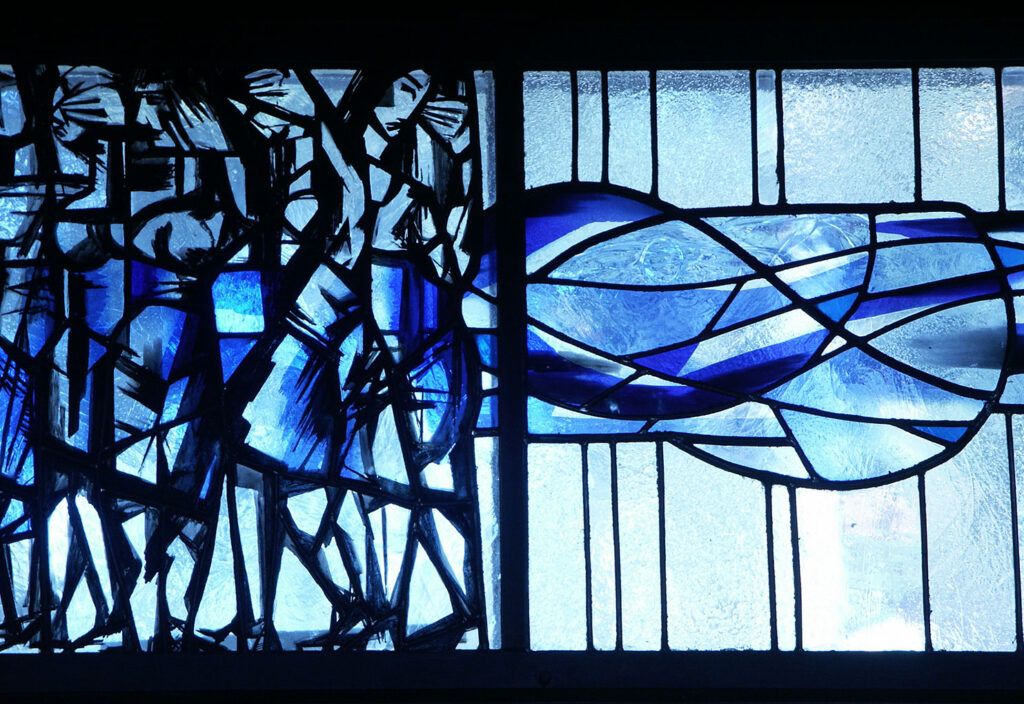 Stained-glass panel with abstract blue waves and dark angular figures on the left, contrasting with a lighter geometric glass design on the right.