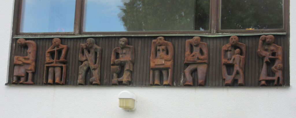 Close-up of a row of cast iron figures mounted on an exterior wall, each depicting stylized seated people in various poses.