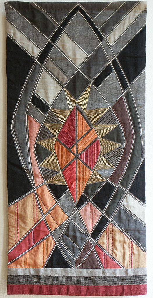 Geometric embroidered wall hanging featuring a bright central star-like shape framed by intersecting stitched patterns in muted colours.