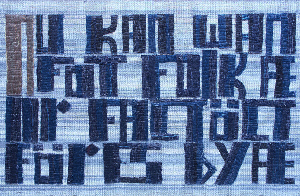 Textile panel with dark woven block-like letters arranged in dense rows on a light blue background.