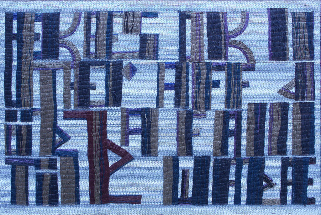 Woven artwork showing tall narrow letter-forms in blue and brown tones on a pale striped textile surface.