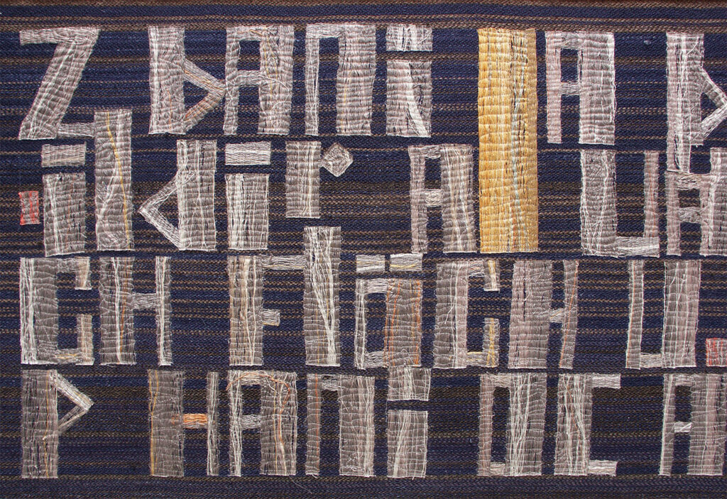 Dark woven tapestry featuring pale blocky symbols and letters arranged in tight rows on a striped background.
