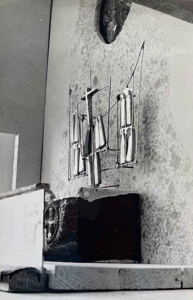 Black-and-white view of a small crucifix sculpture mounted on a patterned wall above a simple altar platform in a minimalist church model.