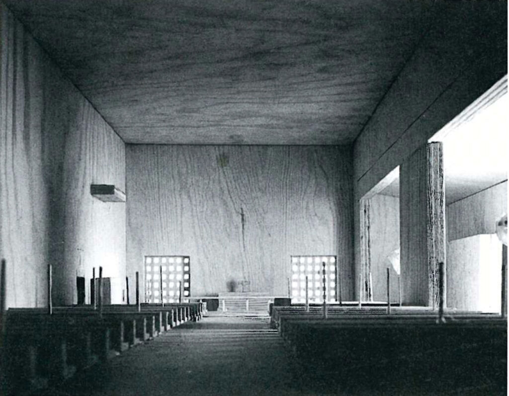 Black-and-white view of a simple wooden architectural model of a church interior with pews, square patterned windows, and a plain altar wall.