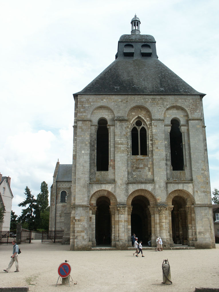 Front view of a large stone church with arched entrances, tall windows, and a steep roof, with people walking in the open courtyard.