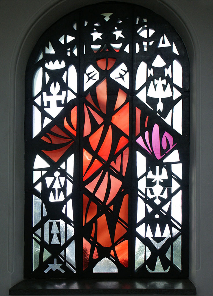 Stained-glass window with intricate black geometric patterns framing a central red and pink abstract figure, set in an arched opening.