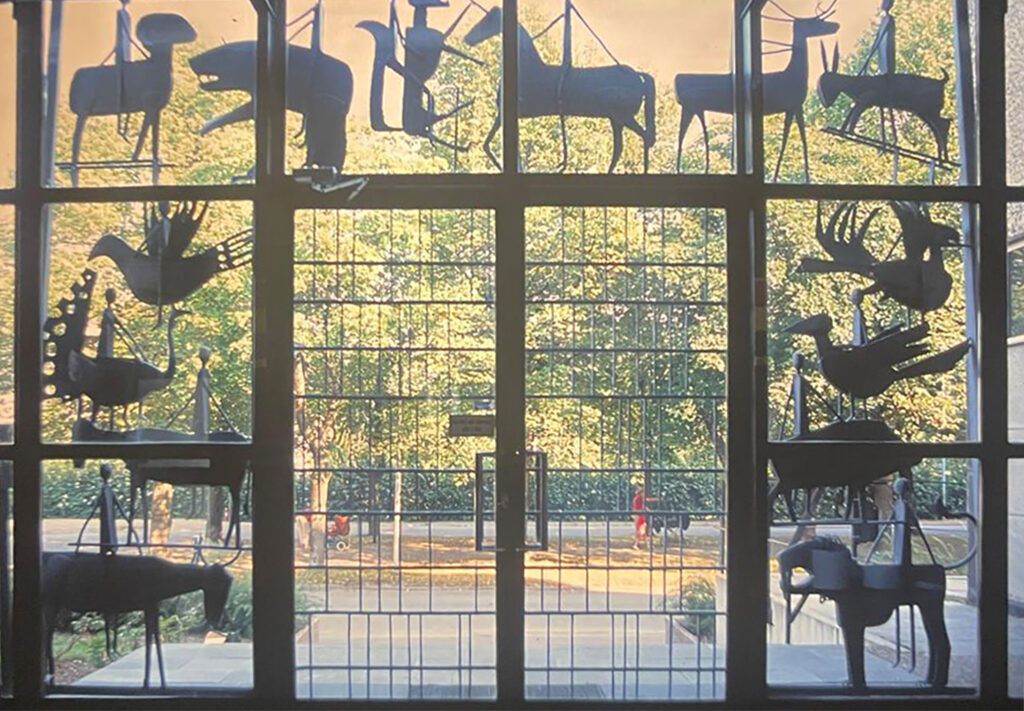 Backlit view from inside a building showing silhouetted metal animal sculptures arranged around a glass entrance door.